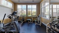 Located at 2525 Crescent View Dr in Charlotte, NC, this well-appointed fitness center offers a comprehensive workout environment designed to meet a wide range of exercise needs. The single-floor facility is bright and inviting, with warm yellow walls and large multi-pane windows that flood the space with natural light and provide pleasant views of the surrounding outdoor greenery.

The strength training area is fully equipped with a selection of Cybex weight machines, including chest press, leg press, and cable stations, as well as a dedicated free weight section featuring a full rack of dumbbells and weight benches. Floor-to-ceiling mirrors line one wall, visually expanding the space and allowing users to monitor their form throughout their workouts.

The cardio zone is lined with modern treadmills and an elliptical machine, all positioned to face the large windows, making workouts more engaging. Durable rubber flooring throughout provides both safety and comfort.

Ceiling fans and recessed lighting ensure a comfortable environment regardless of the time of day. The layout is thoughtfully organized to allow for easy movement between equipment zones. A wall-mounted television adds convenience for entertainment during workouts. This fitness center presents a clean, functional, and energizing space well-suited for daily exercise.