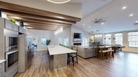 Located at 911 Heron Springs Pkwy in Stow, Ohio, this well-appointed single-floor community clubhouse offers a thoughtfully designed, open-concept layout across a generous footprint. The main gathering area is anchored by soaring vaulted ceilings with exposed wood beam accents, wood-look plank flooring, and a sleek linear fireplace set into a floor-to-ceiling tile feature wall with a mounted flat-screen TV above. Ceiling fans throughout ensure comfort year-round. The fully equipped kitchen features gray shaker-style cabinetry, quartz countertops, stainless steel appliances including double wall ovens and a full-size refrigerator, and a striking blue-and-gray mosaic tile backsplash. A large central island with pendant lighting provides additional seating and workspace. The game room hosts a billiard table beneath pendant lighting, with ample natural light streaming through multiple windows. A dedicated business center offers a conference table with seating, individual computer workstations, open shelving, and a lounge chair — ideal for remote work or meetings. A separate package room is lined with secure lockers for convenient parcel management. Two bathrooms and a closet round out the functional amenities of this vibrant community space.