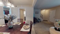 Located at 4031 7 Oaks Ln in East Point, Georgia, this two-story home offers a well-designed layout with comfortable, functional living spaces throughout both floors. The main level features a spacious living room with plush carpeting, a curved sectional sofa, and a large window that brings in natural light. The living area flows seamlessly into a formal dining room, defined by a step-down design and illuminated by an elegant chandelier overhead. A decorative console and accent pieces create a warm transition between the two spaces. The kitchen is well-appointed with rich dark cabinetry, granite-style countertops, a double stainless steel sink, tile flooring, and black appliances. Adjacent to the kitchen is a cozy breakfast nook with a high-top table and natural light from a side window. A half bathroom on the main level features a dark wood vanity with stone-style countertops and tile flooring. Upstairs, the primary bedroom is generously sized with soft carpet, a textured ceiling, and a private en-suite bath. An additional room offers versatile space suitable as a bedroom or sitting area, complete with a window overlooking the outdoors. Throughout the home, neutral tones and warm finishes create a cohesive and inviting atmosphere.
