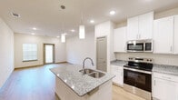 Located at 691 Union Chapel Rd in Cedar Creek, TX, this single-story, one-bedroom, one-bathroom unit offers a thoughtfully designed open-concept layout that maximizes its compact footprint. The combined kitchen and living area serves as the heart of the home, featuring light hardwood flooring that extends throughout the main living spaces and contributes to a bright, clean aesthetic.

The kitchen is well-appointed with crisp white shaker cabinetry, granite stone countertops, and a central island with a double-basin stainless steel sink and pendant lighting overhead. A full suite of stainless steel appliances—including a refrigerator, electric range, and built-in microwave—completes the functional cooking space. The living area flows naturally from the kitchen toward a front entry door flanked by windows, allowing natural light to fill the space.

The bedroom offers a comfortable and private retreat, finished with plush carpeting, a ceiling fan, and a window with blinds. A dedicated closet provides convenient storage. The bathroom includes a tub/shower combination with white tile surround, a granite-topped vanity with white cabinetry, and hardwood-style flooring. Throughout the unit, neutral wall tones and clean finishes create a modern, move-in-ready environment.