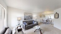 This well-appointed one-bedroom, one-bathroom residence in Sterling Heights, Michigan offers a thoughtfully designed single-floor layout that maximizes functionality and comfort. The combined living and dining area forms the heart of the home, featuring neutral-toned carpet, bright white walls, and large windows that invite natural light throughout the space. The living room provides generous room for seating and entertainment, while the adjacent dining area is defined by a stylish pendant chandelier and a half-wall pass-through that connects visually to the kitchen, enhancing the open feel of the space. The galley-style kitchen is efficiently designed with white cabinetry, granite-toned countertops, stainless steel appliances including a refrigerator and microwave, and tile flooring. The spacious primary bedroom features plush carpeting, clean white walls, and direct access to a closet. Two additional closets throughout the unit offer exceptional storage capacity. The combined bathroom and laundry room includes a full tub-shower combo, a vanity with granite-style countertops, tile flooring, and a large mirror. With three closets and a practical, cohesive design, this residence delivers comfort and convenience in a quiet Sterling Heights location.