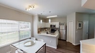 Located at 4200 Northern Cross Blvd in Haltom City, Texas, this single-story residence offers a well-designed, functional layout with a clean, contemporary aesthetic throughout. The open-concept kitchen and dining area serves as the heart of the home, featuring white shaker-style cabinetry, light quartz countertops, a gray subway tile backsplash, stainless steel appliances including a refrigerator and microwave, and a peninsula with an undermount sink. Pendant lighting and a nearby dining area with natural light from a large window complete the space. The living area provides a comfortable retreat with neutral walls and room for relaxed seating arrangements. The bedrooms offer plush carpeting, natural light through slatted blinds, and ceiling fan fixtures, creating a calm and restful atmosphere. The bathroom includes a full tub and shower combination with clean white tile surround. A dedicated in-unit laundry closet houses a full-size washer and dryer alongside a water heater, adding everyday convenience. Dark wood-style flooring flows through the main living areas, tying the space together with a cohesive, modern look. The overall ambiance is bright, neutral, and move-in ready.