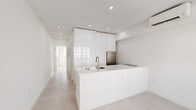 Located at 710 Seventh St in Miami Beach, FL, this thoughtfully designed one-bedroom, one-bathroom residence offers a clean, modern aesthetic defined by an all-white palette and high-quality finishes. The open-plan living and kitchen area serves as the heart of the unit, anchored by a streamlined white kitchen island equipped with an undermount sink and brushed nickel faucet. Floor-to-ceiling high-gloss cabinetry maximizes vertical storage, while a stainless steel refrigerator and built-in cooktop complete the functional kitchen layout. Recessed lighting throughout ensures consistent, bright illumination, complemented by a wall-mounted mini-split system for climate control. Light-toned large-format tile flooring runs throughout the living areas, contributing to the cohesive, airy feel of the space. A hallway connects the main living area to the private bedroom, which features a built-in closet with sliding doors, a wall-mounted mini-split unit, and a window that invites natural light. The bathroom is finished to a high standard, showcasing marble-look wall tiles, a glass-enclosed walk-in shower with a rainfall showerhead, a white floating vanity with gold-toned hardware, and neutral flooring. The overall ambiance is minimalist and refined, well-suited for modern urban living in Miami Beach.