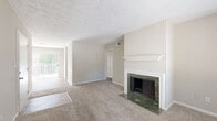This single-floor residence offers a well-organized layout combining comfortable living spaces with practical design. The living room serves as a central gathering area, highlighted by a standout fireplace framed in green marble with a classic white mantel surround—an elegant focal point set against neutral-toned walls and plush carpeting. Natural light enters through a sliding glass door, adding brightness to the open feel of the space.

The kitchen features white shaker-style cabinetry, a white subway tile backsplash, gray countertops, and wood-look vinyl flooring. Black appliances, including a range, dishwasher, and refrigerator, provide a bold contrast to the clean white finishes. A window above the sink allows natural light to filter in.

The bedrooms are carpeted and neutrally painted, each equipped with ceiling fans for ventilation. The primary bedroom includes a closet and direct access to a bathroom. Additional bedrooms offer windows with natural views and ample floor space. The bathroom is outfitted with a single-sink vanity featuring dark countertops, a tiled tub-shower combination, and wood-look flooring. Throughout, textured ceilings and clean white trim add consistent architectural detail.