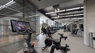 Located at 951 Fell St in Baltimore's vibrant Harbor East neighborhood, this contemporary fitness center offers a well-appointed, single-floor layout designed to support a wide range of workout routines. The space features a striking industrial-modern aesthetic, with a dark exposed ceiling accented by linear LED lighting that illuminates the floor throughout. Neutral-toned carpet tiles cover the flooring, contributing to a clean and professional environment.

The cardio zone is lined with an impressive row of treadmills, ellipticals, StairMaster climbers, and interactive cycling bikes equipped with screen displays for on-demand classes. Floor-to-ceiling glass partitions divide sections of the facility, adding visual openness while defining distinct workout areas. Large windows along the perimeter allow natural light to fill the space and provide views to the outdoors.

The strength training area includes a Smith machine, cable stations, Precor equipment, TRX suspension systems, a wall-mounted stall bar, and a well-stocked dumbbell rack ranging across multiple weights. Rowing machines, stability balls, medicine balls, resistance bands, and yoga mats round out the functional fitness offerings. Full-length mirrors are strategically placed throughout, enhancing the sense of space and supporting proper form. Changing room access is also available within the facility.
