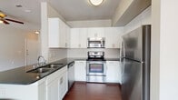 This single-floor residence offers a thoughtfully designed layout that balances functionality and comfort. The kitchen is a standout feature, showcasing white shaker-style cabinetry, dark granite countertops, a classic white subway tile backsplash, and a full suite of stainless steel appliances including a range, over-the-range microwave, and refrigerator. Rich dark hardwood-style flooring anchors the kitchen and extends into the adjacent areas, providing a striking contrast to the cabinetry.

The open living area is bright and inviting, with plush neutral carpeting, a ceiling fan, and large sliding glass doors fitted with vertical blinds that lead to an outdoor view of a pool courtyard, allowing for excellent natural light. A secondary window brings additional light into the connected dining or flex space.

The bedrooms are generously sized, each featuring soft carpeting, ceiling fans, and ample natural light from window treatments. One bedroom includes access to a walk-in closet. The bathroom is finished with dark granite countertops, white cabinetry, and rich dark hardwood-style flooring that ties the space together cohesively.

Overall, the residence presents a clean, modern aesthetic with consistent finishes throughout, creating a comfortable and stylish living environment.