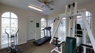 This single-floor fitness room offers a practical and inviting space for exercise and wellness. The room is characterized by elegant arched windows fitted with blinds, which allow generous amounts of natural light to fill the space while maintaining privacy. A ceiling fan overhead ensures consistent airflow and comfort during workouts.

The flooring features a durable, patterned carpet designed to withstand the demands of a fitness environment. The room is equipped with key exercise machines, including a treadmill for cardiovascular training and a multi-function strength training unit, providing users with a well-rounded workout experience.

The walls are finished in a clean, neutral tone, contributing to a bright and focused atmosphere. A paneled entry door with an arched transom window adds an architectural charm to the space. The overall layout is thoughtfully arranged to maximize usability while keeping the environment open and uncluttered. Natural light from multiple windows creates an uplifting ambiance, making this fitness room a functional and pleasant setting for daily exercise routines.