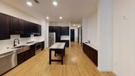 Located on Barclay Downs Drive in Charlotte's desirable 28209 zip code, this single-floor residence showcases a contemporary design with a cohesive palette of crisp white walls, warm hardwood-style flooring, and bold dark cabinetry with gold hardware accents throughout. The expansive kitchen is a standout feature, equipped with dark shaker-style cabinetry, stainless steel appliances including a French door refrigerator and range, a marble-topped island, a subway tile backsplash, and recessed lighting — creating a functional and visually striking culinary space. A secondary prep sink adds further convenience. The bedrooms are generously sized, each featuring ceiling fans, large windows with roller shades that invite natural light, and views of the surrounding greenery and neighborhood. Closets are well-appointed, including a spacious walk-in with built-in rods. The bathrooms are finished to a high standard, featuring dark-framed mirrors, marble-look countertops, dark vanity cabinetry with gold pulls, matte black fixtures, and light tile flooring. A soaking tub and separate shower are present in the main bathroom. A powder room with its own vanity offers added convenience. A sliding barn door and consistent black interior doors reinforce the modern aesthetic throughout the home.