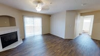 This single-story space features a well-appointed main living area that combines functionality with comfortable design. The room is anchored by rich, dark hardwood-style flooring that runs throughout, creating a warm and cohesive aesthetic. A sliding glass door dressed with vertical blinds serves as a prominent architectural feature, flooding the space with natural light while providing direct access to an outdoor area, offering pleasant views and ventilation options. The textured ceiling adds subtle visual interest overhead, complemented by a decorative pendant light fixture that provides ambient illumination to the room. Neutral-toned walls offer a versatile backdrop, making the space adaptable to a variety of interior design styles. A visible entryway or transition point along one wall hints at additional rooms or storage beyond the main living area. The open layout of the main room contributes to an airy, uncluttered feel, and the combination of natural light and warm flooring tones gives the space an inviting and practical character suitable for everyday living.