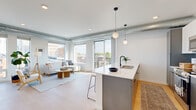 Located at 304 N Second St in downtown Mankato, MN, this thoughtfully designed unit blends modern aesthetics with industrial character. Exposed metallic ductwork runs throughout the ceilings, complementing the clean white walls and light-toned hardwood flooring that flow seamlessly across the space.

The open-concept kitchen and living area serves as the heart of the unit. The kitchen features a large peninsula with a white quartz countertop and bar seating for multiple guests, sleek two-tone cabinetry in white and dark gray, stainless steel appliances, and globe pendant lighting. The adjacent living area is bathed in natural light from oversized windows and a sliding glass door that opens to a private balcony, offering sweeping views of the Mankato cityscape.

The bedroom includes a tall window framing urban views, while the dedicated office provides a bright, productive workspace with its own large window overlooking the city. Two full bathrooms feature modern dark-hardware fixtures, light wood flooring, and clean white cabinetry. A hallway with a closet adds practical storage. The unit's industrial-modern design, abundant natural light, and downtown location make it a distinctive and functional living space.
