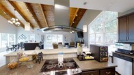 Located at 7303 Hihenge Ct in Raleigh, NC, this single-floor community space is designed to be both functional and inviting. The interior is highlighted by striking vaulted ceilings clad in warm wood planking, supported by exposed beams that add a rustic yet modern character to the space. Track lighting runs along the ceiling, complementing the natural light that floods in through large windows overlooking a tree-lined exterior.

The kitchen area is well-appointed, featuring a stainless steel electric cooktop and a bold curved glass range hood that serves as a central design statement. Granite countertops provide ample workspace, and a refreshment station with a coffee and beverage setup makes the area ideal for hosting and hospitality. A tiled backsplash adds a clean, polished finish to the kitchen.

Adjacent to the kitchen, the open lounge area offers a comfortable seating arrangement with upholstered chairs and accent tables, creating a relaxed gathering environment. A wall-mounted television is positioned for easy viewing from the lounge. The seamless flow between the kitchen and lounge areas makes this space well-suited for community events, meetings, or casual socializing. Overall, the space combines warm architectural details with modern amenities for a welcoming atmosphere.