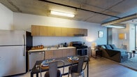 Located at 1522 Gordon St in the heart of Hollywood, Los Angeles, this single-floor urban unit showcases a striking industrial-modern aesthetic defined by exposed concrete ceilings with visible ductwork and piping. The open-plan layout seamlessly connects the kitchen, dining, and living areas into one cohesive space.

The fully equipped kitchen features warm wood-tone cabinetry spanning the full length of the wall, stainless steel appliances including a refrigerator, dishwasher, and gas range, and a clean countertop with an undermount sink. A dark-topped dining table with industrial metal chairs sits adjacent to the kitchen, ideal for everyday meals or entertaining.

The living area is anchored by a large sectional sofa and anchored by a floor-to-ceiling window wall that frames sweeping views of the Hollywood Hills and surrounding neighborhood, flooding the space with abundant natural light. The exposed HVAC ductwork adds to the loft-inspired character of the room.

The bathroom is clean and functional, featuring a wood-toned vanity with under-sink storage, a mirror, and a shower-tub combination. Light wood-style flooring runs throughout the unit, complementing the neutral wall tones and creating a warm, cohesive atmosphere.
