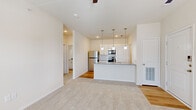 This single-story, one-bedroom, one-bathroom unit offers an efficiently organized layout across a compact but functional footprint. The open-concept living and kitchen area serves as the heart of the unit, where light-toned walls and a seamless transition between wood-look flooring in the kitchen and plush carpet in the living area create a clean, contemporary aesthetic. The kitchen is equipped with stainless steel appliances, including a refrigerator, range, and microwave, complemented by white cabinetry with a subway tile backsplash and a peninsula island featuring a gray quartz-style countertop, an undermount sink, and pendant lighting overhead. The living area benefits from a ceiling fan, carpeted flooring, and a glass-panel door providing both natural light and outdoor access, alongside an additional window with blinds. The bedroom is a comfortable, well-proportioned room with carpet, a ceiling fan, two windows offering natural light, and a dedicated closet. Two hallways connect the spaces efficiently. The bathroom includes a tub-shower combination with white subway tile surround, a vanity with a gray countertop, white cabinetry, and warm wood-look flooring, completing the unit's clean, modern interior palette.