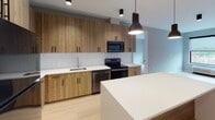 The Vestry is a contemporary 2-bedroom, 2-bathroom residence located in Montclair, NJ, offering a thoughtfully designed single-floor layout with modern finishes throughout. The kitchen is a standout feature, showcasing warm wood-toned cabinetry with matte black hardware, white quartz countertops, a subway tile backsplash, and a full suite of black stainless steel appliances. A kitchen island provides additional prep and gathering space, while pendant lighting adds a stylish touch. Light wood-style flooring runs throughout the main living areas, enhancing the bright and airy atmosphere. Both bedrooms are well-proportioned, featuring large windows with roller shades that frame views of the Montclair streetscape and allow ample natural light to fill the rooms. The two bathrooms are distinctly appointed: one features a wood-toned vanity, white quartz countertop, large mirror, and dark tile flooring, while the second offers light wood-look tile floors and a tub/shower combination with rich navy blue tile surround and matte black fixtures. An in-unit stacked washer and dryer adds everyday convenience. Neutral gray walls and clean architectural lines give the entire residence a cohesive, contemporary aesthetic suited for modern living.