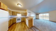 Located at 1010 River Trail Cir in Kiel, Wisconsin, this well-appointed 2-bedroom, 2-bathroom residence offers a comfortable and functional layout across a single floor. The open-concept main living area is a highlight of the home, featuring vaulted ceilings that lend an airy feel to the combined kitchen, dining, and living space. The kitchen is equipped with warm oak cabinetry, a full suite of white appliances including a range, dishwasher, and refrigerator, and a peninsula counter that provides a natural transition into the dining and living areas. Durable hardwood-style flooring runs throughout the kitchen and main entry, while plush carpeting extends through the living room and bedrooms. A ceiling fan with light kit adds both comfort and ambiance to the main living area, which opens to a private balcony through sliding glass doors, offering outdoor views of the surrounding neighborhood. The primary bedroom is generously sized and features a closet, natural light from large windows, and an en-suite bathroom with an oak vanity and tile flooring. The second bedroom also offers ample space and a closet. A dedicated laundry room and a hallway connecting the bedrooms and bathrooms round out this practical and inviting floor plan.
