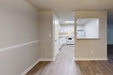 This single-floor residence offers a clean, updated interior with a neutral color palette and a practical layout. The living area is finished with medium-toned wood-style flooring and features a glass-paneled door that admits natural light, creating a bright and open atmosphere. A textured ceiling and crisp white baseboards are consistent throughout the main living spaces.

The kitchen is well-appointed with white shaker-style cabinetry, granite countertops, a subway tile backsplash, and white appliances including a refrigerator and electric range. A pass-through window connects the kitchen to the adjacent living or dining area, enhancing the sense of openness and allowing for easy interaction between spaces. Light wood-style flooring continues through the kitchen.

The bedroom features soft carpeting underfoot, two windows that provide ample natural light and outdoor views, and a ceiling fan for added comfort. Additional rooms include a carpeted space with hallway access to a closet and adjoining areas.

The bathroom is finished with granite countertops, a white undermount sink, white cabinetry, and a full tub-shower combination clad in classic white subway tile, offering a cohesive and well-maintained aesthetic throughout.