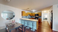 This single-floor residence offers a thoughtfully designed layout that balances open-concept living with defined private spaces. The kitchen serves as a central highlight, featuring warm honey-toned cabinetry, granite countertops, a mosaic tile backsplash, and black appliances including a range and built-in microwave. A peninsula with a granite surface and seating for multiple bar-height stools extends into the dining area, making it ideal for casual dining and entertaining. Rich hardwood flooring flows throughout the kitchen and dining space, complemented by track lighting overhead.

The living room is generously proportioned, with wide sliding glass doors that flood the area with natural light and provide outdoor views and patio access. Vertical blinds offer privacy when desired, and the hardwood flooring continues throughout.

The primary bedroom features plush carpeting, a bright window with an outdoor view, a ceiling fan, and access to a spacious walk-in closet with wire shelving on multiple walls. A second bedroom, also carpeted, includes a large window and a standard closet, making it suitable as a guest room or home office.

The bathroom is clean and functional, with warm-toned tile flooring, a wide vanity featuring granite counters, and wood cabinetry with sleek hardware. The overall ambiance is bright, modern, and move-in ready.