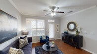This single-story unit in Humble, Texas offers a thoughtfully designed open-concept layout that maximizes functionality and comfort. The living area features rich hardwood-style flooring, crown molding, and a ceiling fan with light fixture. Large windows with blinds flood the space with natural light while providing views of the surrounding exterior, and a private entry door opens directly into the room, adding convenience.

The kitchen is a standout feature, showcasing dark espresso cabinetry that extends to the ceiling, contrasting white countertops, and a spacious island with a built-in sink and bar seating for multiple guests. Black appliances, including a refrigerator, range, and microwave, complement the cabinetry, while track lighting overhead ensures ample illumination. Open shelving nearby provides additional storage and display space.

The bedroom is a calm retreat finished with plush carpeting, crown molding, a ceiling fan, and a window offering pleasant outdoor views. The full bathroom includes a tub-shower combination with tile surround and connects directly to a walk-in closet, offering practical storage. Throughout the unit, a neutral gray palette creates a cohesive and inviting atmosphere.