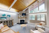 Located at 414 Point Return Dr in Ballwin, Missouri, this single-floor community space offers an open, airy atmosphere defined by its dramatic vaulted ceiling clad in warm natural wood planks and accented by white structural beams. The soaring roofline peaks at an impressive height, creating a grand sense of volume throughout the main living area. Large floor-to-ceiling windows at the front of the space flood the interior with abundant natural light and provide views of the surrounding greenery, enhancing the connection to the outdoors.

The living room serves as the centerpiece of the space, anchored by a striking floor-to-ceiling stacked stone corner fireplace with a wooden mantel and wall-mounted television. Comfortable seating arrangements, patterned carpet flooring, and warm accent décor contribute to a relaxed yet polished ambiance. A dedicated workstation area with built-in desk space lines the windowed wall, offering functional workspace within the open layout. A coffee station and reception desk near the entrance provide a welcoming arrival experience.

The kitchen features crisp white shaker cabinetry, light granite countertops, a classic subway tile backsplash, and hardwood flooring — delivering a clean, modern aesthetic that complements the warmth of the main gathering area.