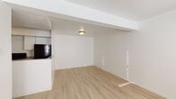 This single-floor unit presents a clean, minimalist aesthetic carried consistently throughout all rooms. Light wood-look flooring extends across the entire space, creating a cohesive and modern foundation. The open living area is defined by crisp white walls, structural beams, and flush-mount ceiling lighting, giving the space an airy, functional feel.

The kitchen is positioned adjacent to the living area and is accessible via a pass-through counter. It features white cabinetry with granite-style countertops, a full suite of black appliances including a refrigerator, electric range, and dishwasher, and ample upper and lower cabinet storage arranged in an efficient L-shaped layout.

The bedrooms are well-proportioned, each featuring windows with blinds that allow natural light to filter in. At least one bedroom includes a built-in closet with bifold doors. The unit contains two bathrooms: one full bath equipped with a tub-shower combination and chrome fixtures, and a second bath featuring a vanity with a granite-style countertop and matching flooring. Both bathrooms maintain the same clean, white palette found throughout the unit.