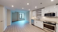 This thoughtfully designed single-floor unit offers a clean, contemporary aesthetic defined by light hardwood flooring, recessed lighting, and a neutral color palette that creates a bright and airy atmosphere throughout. The open-concept layout seamlessly connects the kitchen and living area, maximizing the sense of space and encouraging easy everyday flow. The kitchen is a standout feature, outfitted with sleek white high-gloss cabinetry, open display shelving, granite countertops, a subway tile backsplash, and a full suite of stainless steel appliances including a refrigerator, range, microwave, and dishwasher. A window in the living area allows natural light to filter into the space, further enhancing the open feel. The bedroom is generously proportioned, offering wall-mounted speaker provisions and access to a dedicated walk-in closet, providing ample storage. The bathroom is finished with consistent attention to detail, featuring a white vanity with granite countertop, tile flooring, a large mirror, and a tiled shower area. Throughout the unit, the cohesive use of white tones, light wood, and modern fixtures creates a polished, move-in-ready environment well-suited for contemporary living.
