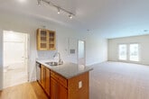 Located at 4375 Regency Dr in High Point, NC, this well-appointed one-bedroom, one-bathroom residence offers a thoughtfully designed single-floor layout that maximizes functionality and comfort. The open-concept kitchen and living area serves as the heart of the home, featuring warm honey-toned cabinetry with glass-front upper cabinets, granite countertops, a stainless steel double sink, a built-in dishwasher, and a stainless steel range with a sleek overhead vent hood. Track lighting illuminates the kitchen, which transitions seamlessly into the carpeted living area. The living room is bright and airy, benefiting from natural light and access to a private balcony through elegant French doors. The generously sized primary bedroom features plush carpeting, neutral walls, and ample space for furnishings. It is accompanied by a walk-in closet outfitted with multi-tiered wire shelving for organized storage. The full bathroom includes a granite-topped vanity with warm wood cabinetry, a framed mirror, tile flooring, and a wall-mounted storage cabinet. Hardwood flooring runs through the kitchen area, while soft carpet extends through the living room and bedroom, creating a cohesive and comfortable living environment throughout.