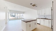 Located at 705 W 9th St in the heart of Downtown Los Angeles, this modern unit offers a thoughtfully designed open-concept layout that seamlessly integrates the kitchen and living areas. Light hardwood flooring runs throughout, complementing the clean, contemporary aesthetic defined by crisp white walls and abundant natural light.

The kitchen is a standout feature, showcasing white shaker-style cabinetry, rich dark countertops, and a classic white subway tile backsplash. A central island provides additional prep and storage space, while a full suite of stainless steel appliances — including a French door refrigerator, wall oven, built-in microwave, and dishwasher — ensures a well-equipped culinary space.

The living area is defined by expansive floor-to-ceiling windows that frame striking panoramic views of the Downtown Los Angeles skyline, flooding the space with natural light and creating a dramatic urban backdrop. A separate room offers a walk-in closet with built-in shelving, with additional floor-to-ceiling windows providing further city views.

The bathroom features stone tile flooring, a white vanity with a dark stone countertop, a large mirror, and a glass-enclosed walk-in shower with white tile surround, delivering a clean and functional finish throughout.