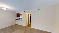 Located at 3300 Shannon Rd in Durham, NC, this two-floor residential space offers a straightforward and functional layout designed for comfortable everyday living. The main living area is finished with wall-to-wall carpeting in a neutral tone, creating a warm and inviting atmosphere throughout. Cream-colored walls and a textured ceiling contribute to a bright, open feel, while multiple HVAC vents ensure climate control across the space.

The kitchen is positioned adjacent to the living area and features dark wood cabinetry, a dark countertop, and a range, offering a compact yet well-equipped cooking space. A pass-through opening connects the kitchen to the living area, promoting an open flow between the two spaces.

A doorway off the main living area leads to an additional room with hardwood-style flooring and built-in shelving, suitable for use as a storage, pantry, or utility space. A staircase connects the two floors, providing access to the upper level of the home. The overall design is clean and practical, with neutral finishes throughout that offer a versatile backdrop for a variety of interior styles. The multi-level layout adds dimension and separation between living zones, making this a well-organized residential space.