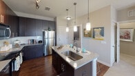 This single-floor residence offers a thoughtfully designed layout that balances modern aesthetics with everyday functionality. The kitchen serves as a central highlight, featuring dark cabinetry, granite-style countertops, a stainless steel appliance suite including a refrigerator, range, and built-in microwave, and a subway tile backsplash. A center island with a stainless steel sink and pendant lighting above creates an ideal space for meal prep and casual dining. Wood-style flooring grounds the kitchen and extends into adjacent areas.

The space includes multiple well-proportioned bedrooms, each finished with plush carpet and ceiling fans. Large windows allow natural light to fill the rooms while offering pleasant outdoor views. Each bedroom is complemented by its own walk-in closet, providing ample storage.

Two bathrooms serve the residence: one featuring a glass-enclosed shower with wood-style flooring and granite countertops, the other offering a full soaking tub with a shower curtain setup. Both bathrooms are finished with rich, calming wall tones and granite vanity counters.

Throughout the residence, neutral wall colors create a clean, cohesive backdrop, while the open-concept kitchen and living area foster a connected and welcoming atmosphere.