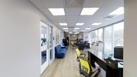 The North Park Apartments leasing office is a thoughtfully designed, single-floor space that balances functionality with a welcoming atmosphere. Upon entering, visitors are greeted by a comfortable lounge area furnished with bold blue seating, providing a relaxed setting for residents and prospective tenants alike. The reception and administrative area features dedicated workstations equipped with modern office furniture, including vibrant yellow-green ergonomic chairs, offering staff an efficient and organized workspace. Large, flush-panel LED ceiling lights illuminate the entire space evenly, contributing to a bright and professional environment throughout. The layout flows naturally from the front reception zone toward the rear of the office, where additional desk space and filing storage support day-to-day operations. Windows along the perimeter allow natural light to filter in, enhancing the open, airy feel of the interior. A glass-paneled door provides direct access to an on-site fitness center, visible from the main office area and equipped with cardio equipment including treadmills. Light hardwood-style flooring runs throughout the space, adding warmth and continuity. Decorative artwork on the walls adds a touch of personality, making the overall environment feel both practical and inviting for all who visit.