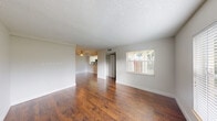 This two-bedroom, two-bathroom two-story home is thoughtfully laid out across two floors, offering a comfortable and functional living environment. The main floor features two living areas, both showcasing rich, warm hardwood-style flooring that flows seamlessly throughout. One living space opens toward the kitchen and includes a ceiling fan, while the other sits adjacent to a carpeted staircase leading to the upper level. Natural light enters through slatted blinds on windows that frame views of surrounding greenery.

The kitchen is well-appointed with white shaker cabinetry, a stone-look countertop with an island, a tile backsplash, and stainless steel appliances including a refrigerator and dishwasher. Light wood-look flooring ties the kitchen and dining area together. A hallway connects the main floor's key spaces, with a full bathroom featuring a tiled tub-shower combination.

Upstairs, the two bedrooms offer a quieter retreat. Both rooms are bright and airy, benefiting from windows with outdoor views. The primary bedroom features warm hardwood-style flooring, while the second bedroom is finished with light ceramic tile. Textured ceilings are consistent throughout the home, complementing the clean, neutral wall tones that provide a versatile backdrop for any décor.