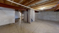 The basement at 1551 Bellora Way in Webster, NY, is a full, unfinished lower level offering a generous open footprint with significant potential for future development. The space features smooth poured concrete flooring throughout, providing a clean and level surface ideal for a variety of uses or future finishing projects.

The overhead structure is fully exposed, revealing the wooden floor joists and subfloor of the level above, along with a prominent structural steel beam that runs the length of the space. Visible throughout the ceiling are organized runs of PEX plumbing lines in red and blue, white PVC drain pipes, and HVAC ductwork, all of which are easily accessible and clearly laid out.

The concrete block perimeter walls are lined with a white plastic moisture barrier, indicating proactive waterproofing measures. A dehumidifier is present, further reflecting attention to moisture management. The electrical panel is mounted along one wall and readily accessible.

A staircase with partial framed walls provides interior access to the main level above. Small egress-style windows allow for limited natural light to enter the space. The basement is divided into two distinct open areas by the central stair enclosure and framing, offering flexibility in how the space can ultimately be utilized or finished.