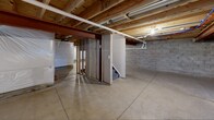 The basement at 1551 Bellora Way in Webster, NY, is a full, unfinished lower level offering a generous open footprint with significant potential for future development. The space features smooth poured concrete flooring throughout, providing a clean and level surface ideal for a variety of uses or future finishing projects.

The overhead structure is fully exposed, revealing the wooden floor joists and subfloor of the level above, along with a prominent structural steel beam that runs the length of the space. Visible throughout the ceiling are organized runs of PEX plumbing lines in red and blue, white PVC drain pipes, and HVAC ductwork, all of which are easily accessible and clearly laid out.

The concrete block perimeter walls are lined with a white plastic moisture barrier, indicating proactive waterproofing measures. A dehumidifier is present, further reflecting attention to moisture management. The electrical panel is mounted along one wall and readily accessible.

A staircase with partial framed walls provides interior access to the main level above. Small egress-style windows allow for limited natural light to enter the space. The basement is divided into two distinct open areas by the central stair enclosure and framing, offering flexibility in how the space can ultimately be utilized or finished.