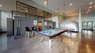 This expansive club room delivers a thoughtfully designed communal space anchored by a distinctive industrial-modern aesthetic. Polished concrete floors run throughout, complementing the high ceilings and contributing to the room's open, loft-like atmosphere. Floor-to-ceiling windows line portions of the exterior walls, flooding the space with natural light and offering views of the surrounding streetscape.

The lounge area features an eclectic mix of mid-century modern seating — including sectional sofas, accent chairs, and layered area rugs — arranged around wall-mounted televisions, with large-scale artwork adding visual interest. A standout element is a vintage Airstream trailer displayed prominently near the billiards area, where a contemporary pool table sits beneath stylish pendant lighting and decorative lattice-panel partitions.

The kitchen and bar area is well-appointed with dark wood countertops, modern bar stools, stainless steel appliances, statement chandeliers, and a coffee station, making it ideal for social gatherings. A dedicated business center offers a conference-style table, desktop computers, and curated wall art beneath a striking sputnik chandelier. Together, these distinct zones create a versatile, vibrant space suited for both relaxation and productivity.