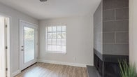 This single-floor, one-bedroom, one-bathroom residence offers a thoughtfully designed layout with modern finishes throughout. Wood-look laminate flooring flows seamlessly across all living spaces, providing a warm and cohesive aesthetic.

The living area is bright and welcoming, featuring a striking floor-to-ceiling tile fireplace surround in a gray tone, a sliding glass door that invites natural light, and a window with horizontal blinds offering views of surrounding greenery. A ceiling fan adds comfort and character to the space.

The kitchen is well-equipped with sleek gray cabinetry, stainless steel appliances including a refrigerator, range, and over-the-range microwave, along with recessed lighting and white countertops. The open pass-through connects the kitchen to the living area, enhancing the sense of space.

The bedroom is generously sized with vaulted ceilings, a ceiling fan with light fixture, and a window that allows ample natural light. It features direct access to both a walk-in closet and the full bathroom, providing convenient and functional flow.

The bathroom is cleanly finished with a dark-framed vanity mirror, white quartz countertop, gray cabinetry, and a shower-tub combination with a white curtain. Wood-look flooring continues into this space, maintaining design consistency throughout the home.