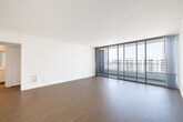 Located at 2800 Neilson Way in Santa Monica, California, this one-bedroom, one-bathroom residence offers a bright and efficient layout with clean, modern finishes throughout. The open-plan living and kitchen area serves as the heart of the home, where light wood flooring flows seamlessly underfoot and crisp white walls create an airy, neutral backdrop. The living area is anchored by a wall of floor-to-ceiling sliding glass doors that open to a balcony, flooding the space with abundant natural light and framing expansive views of the surrounding cityscape and mountains beyond. The kitchen is well-appointed with white cabinetry featuring glass-front upper panels, stone-look countertops, stainless steel appliances including a refrigerator, electric range, and built-in microwave, as well as a peninsula that provides additional prep and dining space. Light tile flooring grounds the kitchen area. The spacious bedroom includes a large window with outdoor views, continuing the light wood flooring found throughout the living areas. A dedicated closet offers practical storage. The bathroom is finished in white tile and features a combination shower and soaking tub, vanity with mirror, and tile flooring. Two hallways provide a clear and organized flow through the residence.