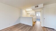 Located at 14543 Burbank Blvd in Los Angeles, CA, this single-floor residence offers a well-organized layout with one bedroom and two bathrooms. The interior is finished in a clean, neutral palette with light wood-style flooring running throughout, creating a cohesive and airy aesthetic.

The living area is open and filled with natural light from a large window that frames views of surrounding greenery, giving the space a bright and inviting character. The kitchen is designed with functionality in mind, featuring a peninsula-style breakfast bar that separates it from the living area. White cabinetry, open upper shelving, and built-in appliances including a microwave and range are neatly arranged within the compact but efficient kitchen footprint. A ceiling-mounted ventilation system is centrally positioned above.

The bedroom is a comfortably sized private retreat with a window that allows natural light to filter in. Its simple, clean walls and wood-style flooring maintain the consistent design language found throughout the unit.

Both bathrooms are practical in design, featuring vanities with warm-toned countertops, under-sink cabinetry, and mirrored storage. The hallway connecting the bathroom area to the kitchen adds to the unit's efficient flow. Overall, the space presents a clean, move-in ready environment suited for comfortable urban living.
