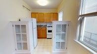Located at 117 North Narberth Avenue in the charming borough of Narberth, PA, this single-floor residence offers a practical and well-organized layout. The kitchen is a central feature of the space, equipped with warm honey-toned wood cabinetry that extends to the ceiling, providing generous storage throughout. White appliances, including a full-size refrigerator and a gas range with oven, are neatly integrated beneath the upper cabinets. A double basin sink sits beneath a window, allowing natural light to filter into the space. The light-toned tile flooring adds brightness to the room and is easy to maintain. Flanking the kitchen entry are two white built-in display cabinets with glass-paned doors, offering both decorative and functional storage while adding a classic architectural detail to the space. The soft yellow-toned walls contribute to a warm, welcoming ambiance throughout. The overall design prioritizes functionality, with a straightforward layout that makes efficient use of the available space on the single floor.