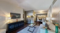 This single-floor residence offers a thoughtfully designed open-concept layout that seamlessly connects the living, dining, and kitchen areas. Rich dark hardwood-style flooring flows throughout the main living spaces, complementing the neutral gray and white color palette that lends a modern, cohesive aesthetic.

The living room is generously proportioned, featuring a wall-mounted flat-screen TV, a media console, and comfortable seating arranged around a glass-top coffee table. It opens directly to the dining area, which is illuminated by an elegant flush-mount chandelier and accommodates a full dining set. A sliding glass door leads to a private balcony, providing outdoor access and natural light.

The kitchen is efficiently laid out in a galley style with white cabinetry, ample counter space, and stainless steel appliances including a refrigerator, microwave, and range. A breakfast bar with barstool seating adds casual dining flexibility.

The bedroom is a calm, carpeted retreat with a walk-in closet. Two full bathrooms each feature a tub-shower combination, white vanity, and matching hardwood-style flooring. A dedicated laundry room with full-size washer and dryer hookups and additional cabinetry rounds out the functional amenities of this well-organized home.