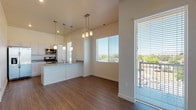 This well-appointed single-floor residence offers a clean, modern aesthetic defined by neutral tones, wood-look plank flooring, and an abundance of natural light. The open-concept living and dining area flows seamlessly into the kitchen, which serves as a functional centerpiece of the home. The kitchen is outfitted with white flat-panel cabinetry, stainless steel appliances including a refrigerator with ice maker, electric range, and built-in microwave, complemented by gray quartz-style countertops and a peninsula with pendant lighting overhead. Large windows with horizontal blinds frame outdoor views and fill the living area with natural light, while a glass door provides access to a balcony. The living space features durable hardwood-style flooring that extends throughout the main areas. The bedrooms are generously sized, finished with plush neutral carpeting and clean white walls, offering a calm and restful environment. The primary suite includes a spacious walk-in closet with full-length hanging rods and carpeted flooring. The bathroom is finished with wood-look tile flooring, a wide vanity with gray countertops and modern cabinetry, and a tub-shower combination. The overall design is contemporary and move-in ready, with a cohesive, light-filled palette throughout.