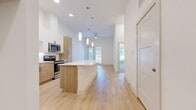 This well-designed one-bedroom, one-bathroom unit offers a thoughtfully arranged open-concept floor plan that maximizes functionality. Light-toned luxury vinyl plank flooring runs throughout the main living areas, complemented by crisp white walls that enhance the bright, airy atmosphere.

The kitchen serves as a focal point, featuring a two-tone design with white upper cabinetry and warm wood-toned lower cabinets, a marble-style tile backsplash, quartz countertops, and a full suite of stainless steel appliances including a refrigerator, range, microwave, and dishwasher. A central island with pendant lighting above provides additional prep space and casual seating. The kitchen flows seamlessly into the living room, which benefits from elevated ceilings, a ceiling fan, and a glass door leading to an outdoor area.

The bedroom is carpeted and generously proportioned, with large windows admitting ample natural light and an adjacent walk-in closet outfitted with built-in shelving and hanging rods. The bathroom features a wood-toned vanity with a white countertop, a glass-enclosed walk-in shower, and light wood-look flooring, maintaining the cohesive modern aesthetic found throughout the unit.