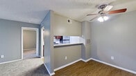 This single-story residence offers a practical and functional layout with a cohesive gray color palette throughout. The living area is carpeted and features a ceiling fan with integrated lighting, providing comfort and airflow. A sliding glass door fitted with vertical blinds allows natural light to fill the space. The living area transitions into a dining zone with hardwood-style flooring, distinguished by a pass-through kitchen window that connects the two spaces visually and functionally.

The galley-style kitchen is well-appointed with dark espresso cabinetry, granite-style countertops, stainless steel appliances including a refrigerator, electric range, and dishwasher, complemented by a tile backsplash and light wood-style flooring. An electrical panel is conveniently located within the kitchen corridor.

The bedrooms are carpeted and painted in soft gray tones, each equipped with ceiling fans and ample closet storage. One bedroom features a built-in closet with bi-fold doors, while a hallway provides access to a full bathroom with wood-style flooring. The textured ceilings and clean white baseboards are consistent throughout, lending the space a uniform and well-maintained character.