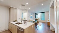 This well-appointed 1-bedroom, 1-bathroom residence offers a thoughtfully designed open-concept layout finished with warm wood-tone flooring throughout. The living area is bright and inviting, anchored by recessed lighting and a large floor-to-ceiling window that frames sweeping panoramic views, flooding the space with natural light. A sleek wood-and-marble console adds a refined decorative touch near the entryway.

The kitchen is modern and functional, featuring light wood cabinetry extending to the ceiling, a white quartz peninsula with an undermount sink, stainless steel appliances including a French door refrigerator, and a tasteful tile backsplash — all seamlessly connected to the living and dining areas.

The bedroom is a calm retreat with a tray ceiling, ceiling fan, and direct access to a generously sized walk-in closet outfitted with built-in shelving, hanging rods, and additional built-in storage with panel doors.

The bathroom is elegantly tiled in soft gray stone-look tile, offering both a soaking tub and a separate glass-enclosed shower, complemented by brushed nickel fixtures and warm vanity lighting. Clean white walls and consistent wood-tone flooring unify the entire residence with a cohesive, contemporary aesthetic.