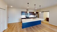 This single-floor unit is thoughtfully designed with a contemporary aesthetic and an efficient, open layout. The kitchen serves as the centerpiece of the space, showcasing a striking large island with a vivid blue base and crisp white countertop, illuminated by a trio of pendant lights. Rich, dark wood cabinetry lines the walls, complemented by white subway tile backsplash and a full suite of stainless steel appliances, including a range, microwave, and refrigerator. A sliding barn door adds a stylish architectural accent nearby, while an in-unit stacked washer and dryer provide added convenience. Light hardwood flooring flows seamlessly throughout the open living areas and into the hallway, connecting the space cohesively. Two well-proportioned bedrooms each feature sliding windows that frame urban rooftop views, with exposed ductwork adding an industrial touch. The unit includes two bathrooms, each finished with white fixtures, a tub/shower combination with curved curtain rod, and dark wood vanities topped with white countertops. The overall ambiance is clean, modern, and functional, balancing bold design accents with neutral tones.