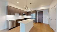 Located at 17371 NE 67th Ct in Redmond, WA, this well-appointed 2-bedroom, 2-bathroom residence offers a thoughtfully designed single-level layout with modern finishes throughout. The open-concept kitchen and living area serves as the heart of the home, showcasing rich dark wood cabinetry, crisp white quartz countertops, a central island with pendant lighting, and a full suite of stainless steel appliances. Light hardwood-style flooring flows throughout the main living areas, lending warmth and continuity to the space. Large floor-to-ceiling windows in the living area and bedrooms flood the interior with natural light while framing pleasant views of the surrounding Redmond treeline and neighborhood. The primary bedroom is generously sized and features its own dedicated closet. Both bedrooms are finished with neutral carpet and oversized windows that continue the home's bright, airy aesthetic. Each bathroom is finished with clean tilework, a soaking tub and shower combination, wood-toned vanity cabinetry, and white quartz counters. A dedicated hallway and entrance provide a practical transition into the home. A wall-mounted mini-split unit ensures year-round climate comfort. The overall ambiance is contemporary, clean, and welcoming.