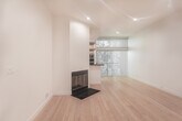 Located in the vibrant Hollywood neighborhood of Los Angeles, this single-floor unit at 7917 Selma Ave offers a clean, modern aesthetic throughout. Light bamboo hardwood flooring runs continuously across the main living areas, creating a warm and cohesive feel that complements the crisp white walls and recessed lighting overhead.

The open living area is generously proportioned, offering a versatile layout with ample wall space and large sliding glass doors that invite natural light and frame lush greenery views from outside. A built-in wood counter or platform element adds a practical and stylish architectural detail to the space.

The kitchen is thoughtfully designed with a galley-style layout, featuring dark quartz countertops, modern light wood cabinetry with open shelving, a stainless steel sink, and stainless steel appliances including a refrigerator and range. Porcelain tile flooring in the kitchen provides a clean transition from the wood floors in the main living area.

The entryway is welcoming and well-lit, with a solid white door and recessed lighting guiding residents into the open floor plan. A dedicated storage area features contemporary frosted glass sliding doors with sleek metal frames, adding both functionality and a refined design touch. The overall ambiance is bright, airy, and minimalist, ideal for those seeking a modern urban retreat.
