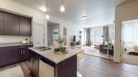 This single-floor residence is designed with a cohesive modern aesthetic, anchored by dark espresso-toned cabinetry, granite countertops, and warm wood-look flooring that carry throughout the main living spaces. The kitchen serves as a central hub, featuring a large island with seating, stainless steel appliances including a refrigerator, range, and built-in microwave, and pendant lighting overhead. Ample upper and lower cabinetry provides generous storage, while the open layout allows the kitchen to flow naturally into the living area.

The living room is bright and spacious, benefiting from large windows dressed with blinds and floor-length drapes that allow for flexible natural light control. The neutral color palette and open layout create an inviting, airy atmosphere.

Two bedrooms offer carpeted flooring and well-sized windows with sheer curtains, providing a comfortable and softly lit retreat. Both bathrooms mirror the home's design language, featuring dark vanity cabinetry, granite countertops, undermount sinks, and large mirrors. The primary bathroom includes a tub-shower combination, while a second full bathroom offers similar finishes. A half bath provides additional convenience for guests.