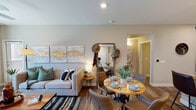 This single-story residence is thoughtfully designed with an open-concept layout that seamlessly connects the living, dining, and kitchen areas. The living room features wood-style flooring, a large window that brings in natural light and outdoor views, a ceiling fan, and neutral-toned walls that complement the contemporary furnishings. A striped area rug and triptych wall art add visual interest to the space.

The adjacent dining area accommodates a round wooden table with upholstered chairs, while a wall-mounted mirror and entryway hooks provide functional organization nearby. The kitchen is well-equipped with rich dark cabinetry, granite countertops, a mosaic tile backsplash, stainless steel appliances, a central island with an undermount sink, and pendant lighting overhead. A dedicated laundry area with a full-size washer and dryer is conveniently accessible from the kitchen.

The bedroom offers plush carpeting, a ceiling fan, a built-in window seat with shelving, and ample natural light. Built-in wall shelves provide additional display and storage space. The bathroom features dark wood vanity cabinetry, granite countertops, a well-lit mirror, and wood-style flooring, maintaining the cohesive design aesthetic found throughout the residence.