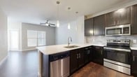 This single-floor residence offers a thoughtfully designed layout with modern finishes and a cohesive aesthetic throughout. The kitchen serves as a central highlight, showcasing dark espresso cabinetry, crisp white countertops, a subway tile backsplash, and a full suite of stainless steel appliances including a range, microwave, dishwasher, and refrigerator. A peninsula with pendant lighting above provides additional workspace and open sight lines into the living area, which features rich wood-look flooring and a ceiling fan. The entryway is clean and functional, with durable wood-look flooring that continues through the main living spaces. Bedrooms are carpeted for comfort, with one featuring an abundance of natural light from multiple windows, including elevated clerestory windows that enhance the sense of height and openness. Additional rooms with wood-look flooring offer versatile usage options. The bathroom is well-equipped with dark cabinetry, a wide vanity with white countertops, a large mirror, and ample storage above. Throughout the space, neutral wall tones, white trim, and consistent hardware finishes create a clean, modern atmosphere that is both practical and inviting.