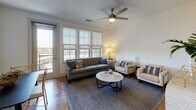 Located in Dallas's vibrant Deep Ellum neighborhood, this single-floor residence offers a thoughtfully designed open layout with contemporary finishes throughout. Warm hardwood flooring flows seamlessly from room to room, tying the space together with a cohesive, inviting aesthetic.

The galley-style kitchen is both functional and stylish, featuring white quartz countertops, a classic subway tile backsplash, a stainless steel appliance suite, and a combination of white upper cabinets and rich wood-toned lower cabinetry. A sliding barn door adds a modern industrial accent near the entryway.

The open living and dining area is bathed in natural light from large floor-to-ceiling windows fitted with roller shades, offering views to the outdoors. A ceiling fan enhances comfort in the spacious living room, which is well-proportioned for both relaxing and entertaining.

The bathroom continues the clean, modern palette with warm wood vanity cabinetry, white countertops, and hardwood-style flooring. An adjacent walk-in closet provides generous storage with built-in shelving and hanging space.

Throughout the residence, the design balances contemporary style with practical livability, creating a bright, well-appointed home in the heart of Dallas.